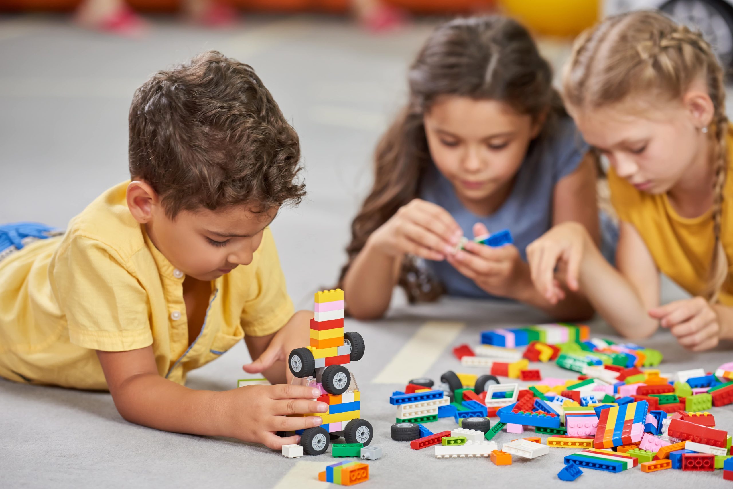 Niños concentrados jugando y construyendo con bloques de construcción coloridos en el suelo.