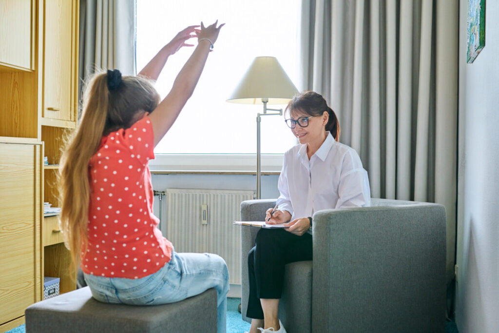Terapeuta infantil femenina hablando con una niña durante una sesión de psicología familiar.