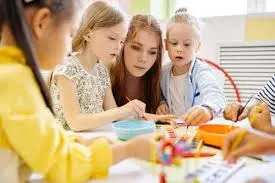 Maestra o tutora asistiendo a varios niños pequeños en una actividad de arte o manualidades en un aula.