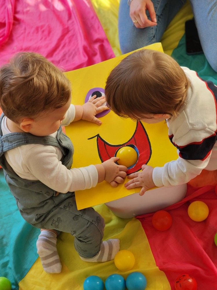 Dos bebés participan en una actividad de estimulación temprana desarrollando la motricidad fina con pelotas de colores.