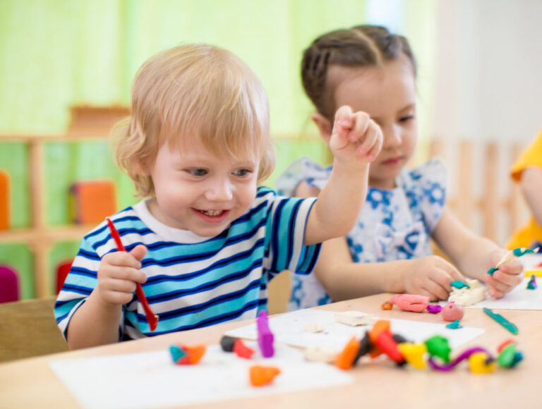 Niño y niña participando en actividad de plastilina para estimulación infantil y desarrollo motor fino.